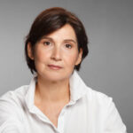 middle aged woman portrait wearing white shirt against gray solid background.